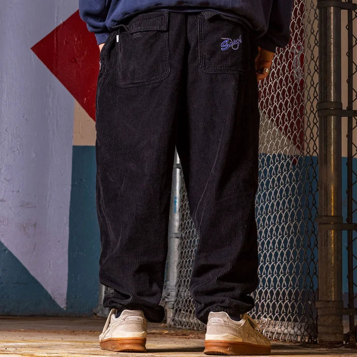 Snack Mic Check Corduroy Pants Black back on model by chainlink fence